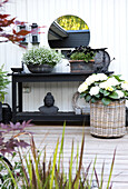 Schwarzer Tisch mit Pflanzen, darüber Spiegel vor weißer Fassade aus Holz