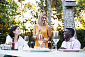 Freunde bei einem sommerlichen Abendessen im Garten öffnen eine Flasche Wein