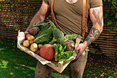 Reifer Mann mit Kiste mit Gemüse in seinem Garten