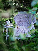 Alte Liegestuhl mit Baumwolldecken und Hocker mit Kaffeegeschirr unter einem Baum