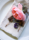 Place setting with old linen cloth as napkin, rose, lavender, and small pieces of wood