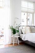 Helles Schlafzimmer mit schwarzem Metallbett und weißem Nachttisch mit Zimmerpflanze