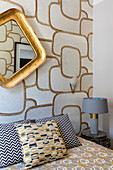 Queen sized bed and gold-framed mirror on a wall with patterned wallpaper