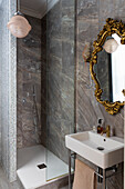 Bathroom sink, antique gold-framed vanity mirror, and a shower stall in bathroom with marble tiles