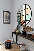 Console with decorative objects, above round wall mirror