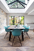 Dining area with glass ceiling, turquoise-colored chairs and view of the garden