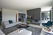 Modernes Wohnzimmer mit grauem Sofa, Sesseln und eingebautem Kamin