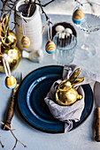 Festive table setting with blue plates and golden bunny on white concrete table