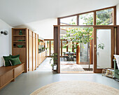 Open-plan interior with low sideboard used as a bench, fitted kitchen with wooden fronts and tree planted in atrium