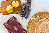 Holzbrett mit Birnen, Lavendelblüte, Strohhut und Buch auf Picknickdecke