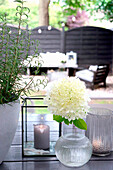 Sitzbereich im Außenbereich mit Hortensien (Hydrangea) und Kerze auf Holztisch