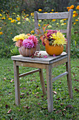 Autumn flowers in hollowed-out pumpkins on an old wooden chair in the garden