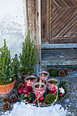 Advent wreath with lanterns, moss, and red apples in a vintage bowl in front of the house entrance