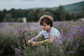 Side view of man with flowers in hand sitting in blooming lavender field and enjoying nature while looking down