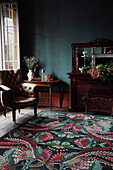 Antique furniture, leather armchair and woollen carpet in room with dark wall