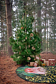 Decorated fir tree, Christmas gifts and round carpet on forest floor