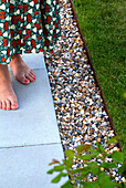 Women's feet on concrete tile next to gravel bed in garden