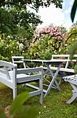 Light grey wooden garden furniture surrounded by blooming roses