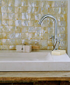 Detail eines modernen Badezimmers mit einem Steinwaschbecken mit verchromtem Wasserhahn und perlmuttfarbenen Fliesen