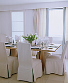 Ein modernes Esszimmer in neutralen Farben mit Holztisch und stoffbezogenen Stühlen mit hoher Rückenlehne, die für das Abendessen gedeckt sind