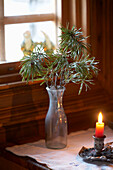 Pine needles in vase with lit candle at window of log cabin in Svartadalen, Sweden
