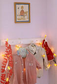 A detail of a row of clothes pegs displaying children's clothes entwined in fairy lights