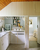 A traditional kitchen with simple units and a row of mugs hanging from the wood panelled ceiling
