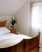 Traditionelles Schlafzimmer Nachttisch aus Holz neben einem Doppelbett mit hölzernem Kopfteil und vor einem mit einem Vorhang bedeckten Fenster