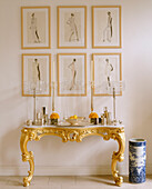 A detail of six framed drawings silver ornaments with glass candleholders on a gold side table next to large blue china pot