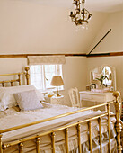 A traditional bedroom with a vintage light suspended above a brass bedstead next to a French dressing table