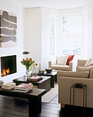 A modern living room with a fireplace underneath a canvas artwork and facing a small coffee table and beige sofas