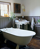 Country style bathroom with a claw foot bathtub ornate sink wood panelling and wood floor