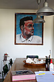 Männerportrait in einem Esszimmer mit Lampenschirmen aus Metall und Künstlerutensilien auf Tisch