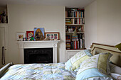 Pillows on antique bed in room with open fireplace and recessed shelving