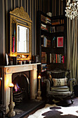 Armchair and corner shelving beside open fire in home of London fashion designer