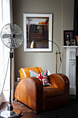 Electric fan and brown leather armchair with Union Jack cushion in home of London fashion designer