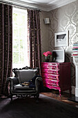 Pink chest of drawers and grey armchair in corner of London fashion designer's home