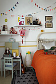 Girlanden, Regale und Bett mit orangefarbenem Überwurf in Kinderzimmer, London