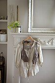 Lace blouse and waistcoat hang on fireplace of London home