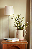 Lampe, Schnittblumen und Buch auf Beistelltisch aus Holz in einem Haus in West Sussex, England, UK