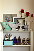 High heeled shoes and cut flowers with artwork on storage shelf in Lincolnshire home, England, UK