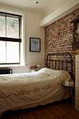 Embroidered cover on bed with exposed brick wall in Brighton home, East Sussex, England, UK
