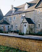 Exterior of a traditionally English Cotswold stone house front porch entrance stone wall attic windows front garden