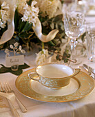 A detail of a traditional dining room place setting with gold tableware soup bowl cutlery wine glass place name tag