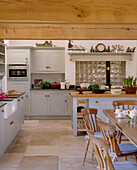 Küche im Landhausstil mit Essbereich, Balkendecke, Steinplattenboden, lackierten Möbel, Kücheninsel, Tisch und Stühlen
