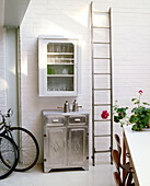 Detail of a porch area with bikes propped up against a wall next to a silver cabinet and a old ladder