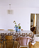 Retro style dining room with floral plastic tablecloth mismatched chairs and perspex hanging light