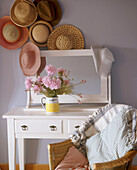 A collection of summer hats hanging above a traditional white wooden dressing table with a mirror and a bunch of flowers on top