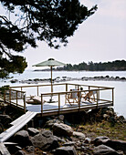 Holzplanken, die zu einer erhöhten Terrasse mit Liegestühlen und einem Sonnenschirm am Rande eines Sees führen