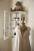 Simple cotton dress on mannequin in front of cupboard with glass shelves
